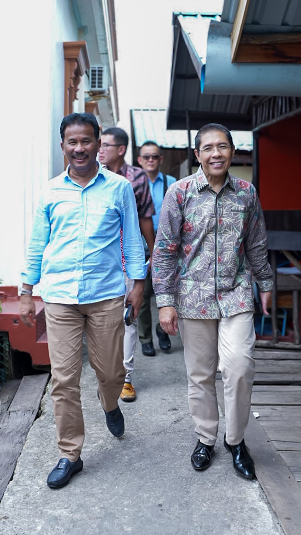 Group of men walk on a sidewalk, wearing casual shirts and slacks.